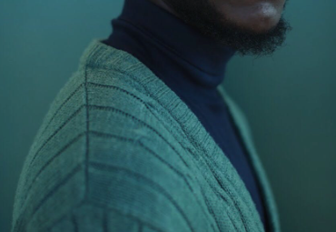 Close-up profile shot of man wearing a green cardigan sweater over a dark turtleneck