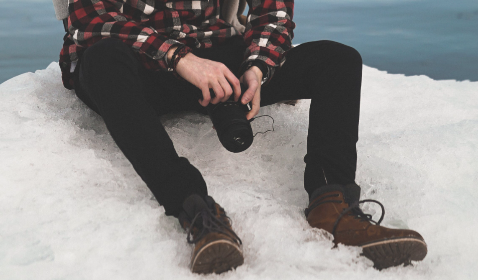 Stylish man sitting in snow with camera.
