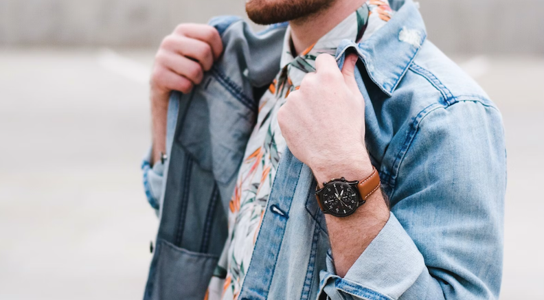 Fashionable man wearing pattered shirt, denim jacket, and a watch.